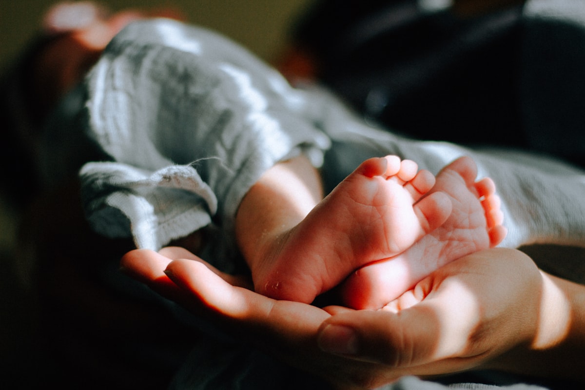 Adult hands gently cradling a baby's bare feet wrapped in a soft organic blanket