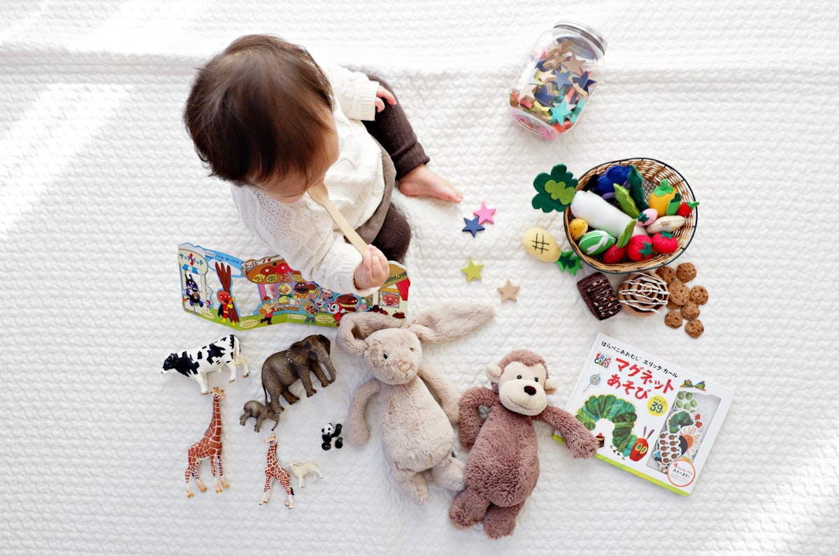 Baby sitting on a blanket surrounded by soft toys and picture books