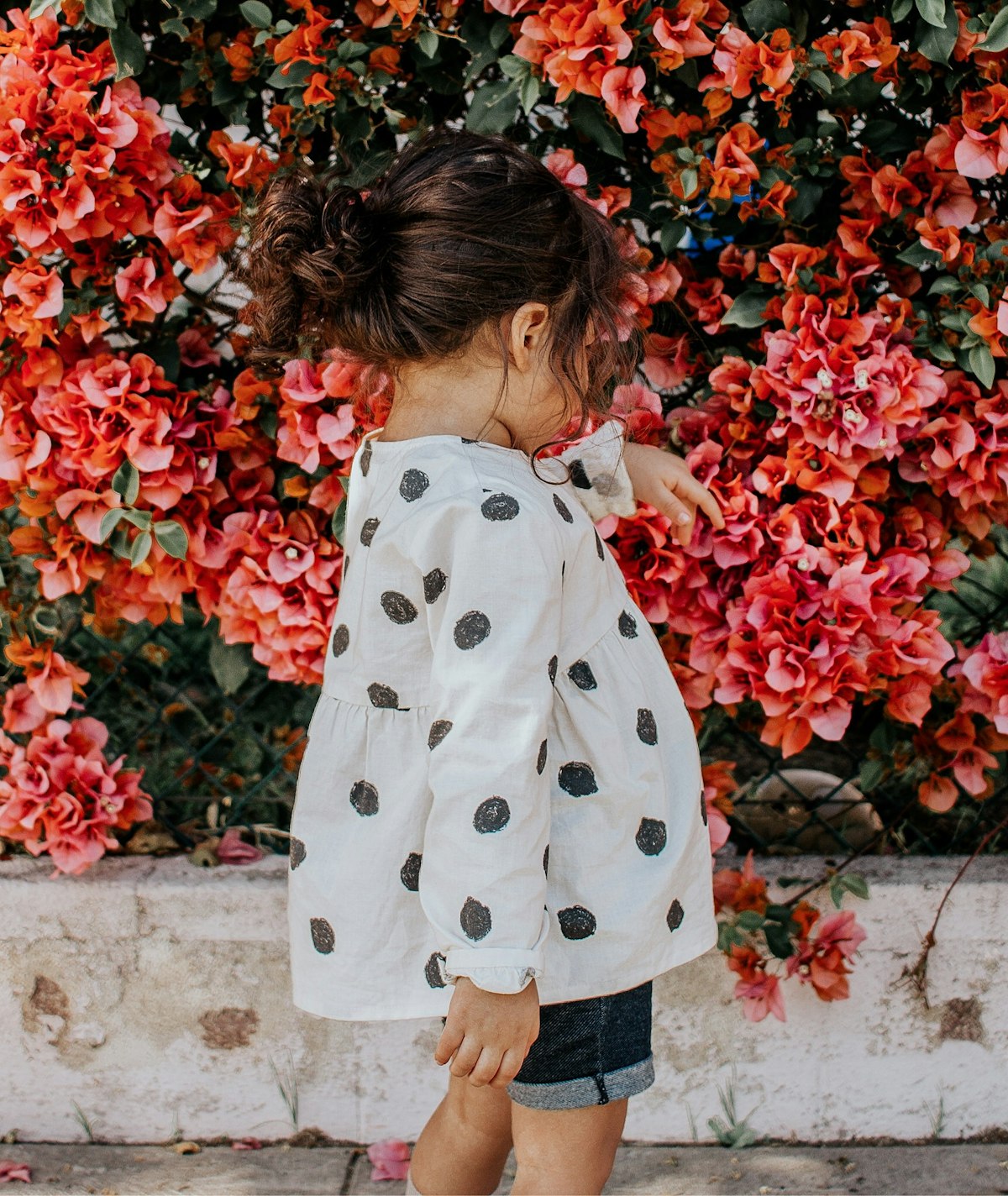 Toddler girl in a polka-dot blouse standing among flowers
