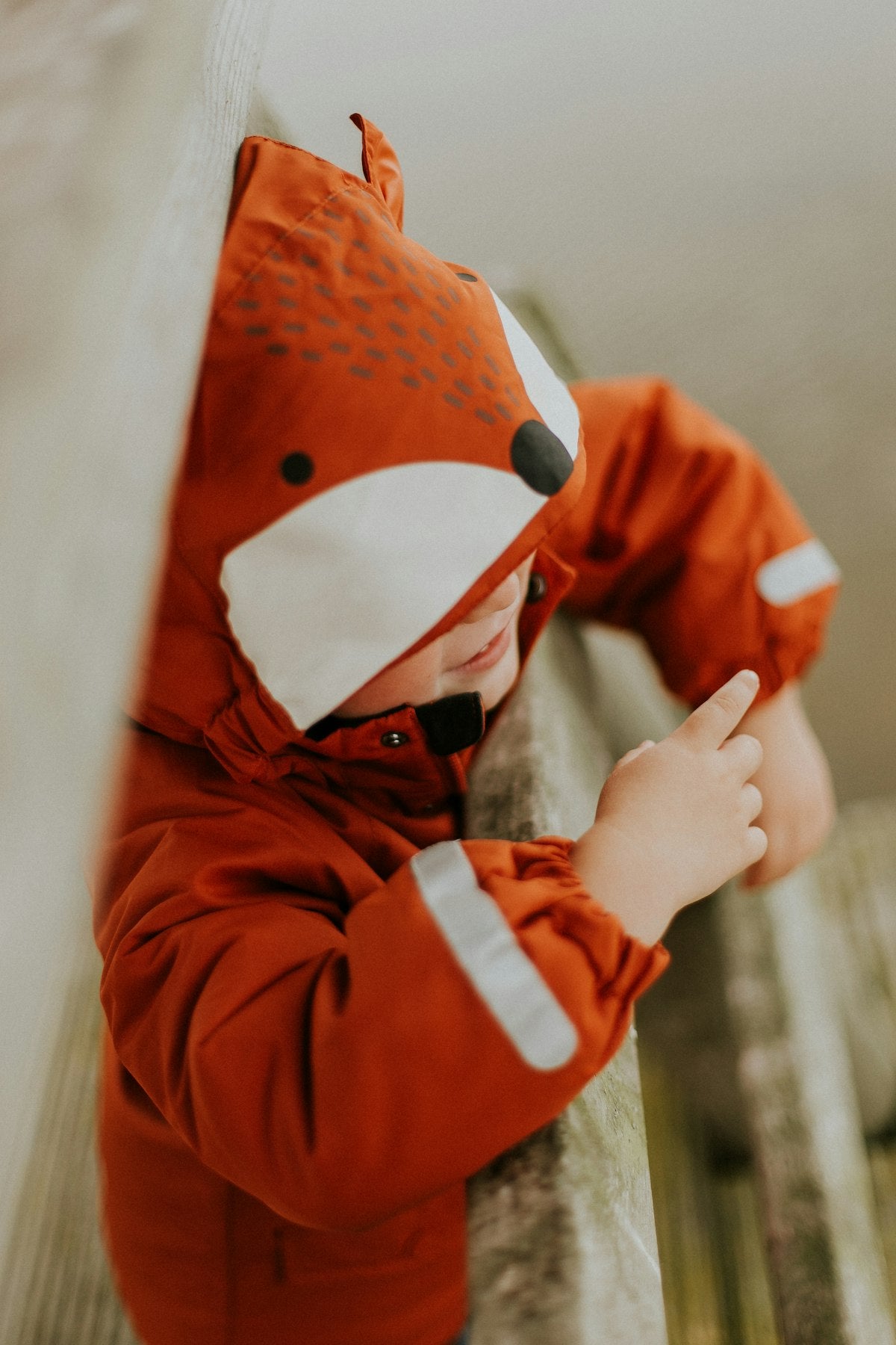 Toddler smiling in a cozy orange fox-shaped jacket, an example of playful gender-neutral style