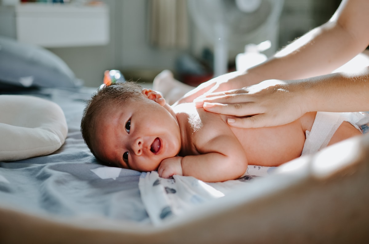 A baby lying on a bed while a woman gently massages their back