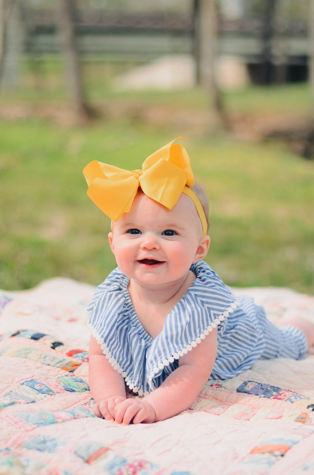 Smiling baby in a simple striped outfit sitting on a quilt, dressed in a toddler capsule wardrobe piece