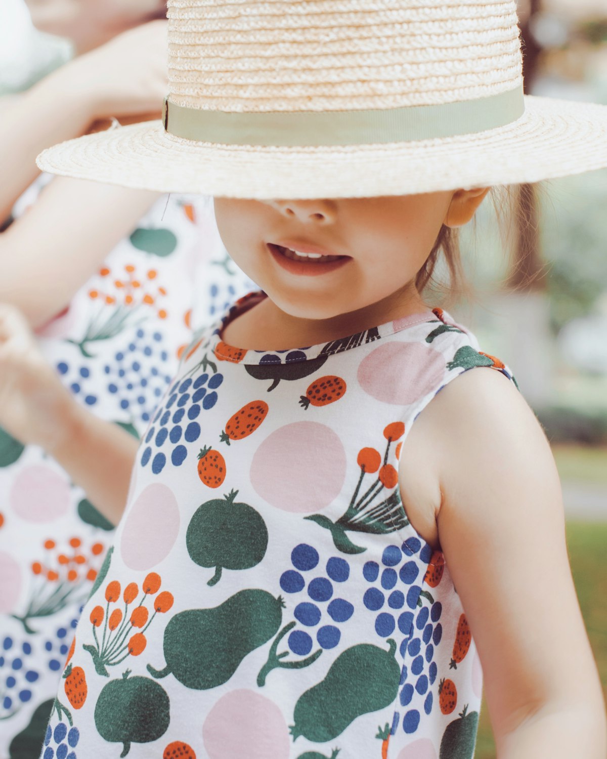 Little girl in a fruit-print dress and sun hat playing outdoors